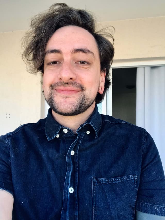 A photo of Sérgio Júnior, with a blue jean tshir. He smiles.